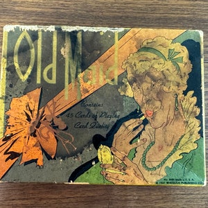 May include: Vintage Old Maid playing card game box with a colorful illustration of a woman with a bow in her hair and a large bow on the front of the box. The box contains 45 cards and is made of card quality.