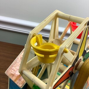 K&ouml;nnte beinhalten: Ein vintage Spielzeug-Riesenrad aus Plastik mit gelben, roten und gr&uuml;nen Sitzen. Das Rad ist wei&szlig; mit schwarzen Akzenten und Teil eines gr&ouml;&szlig;eren Spielsets.