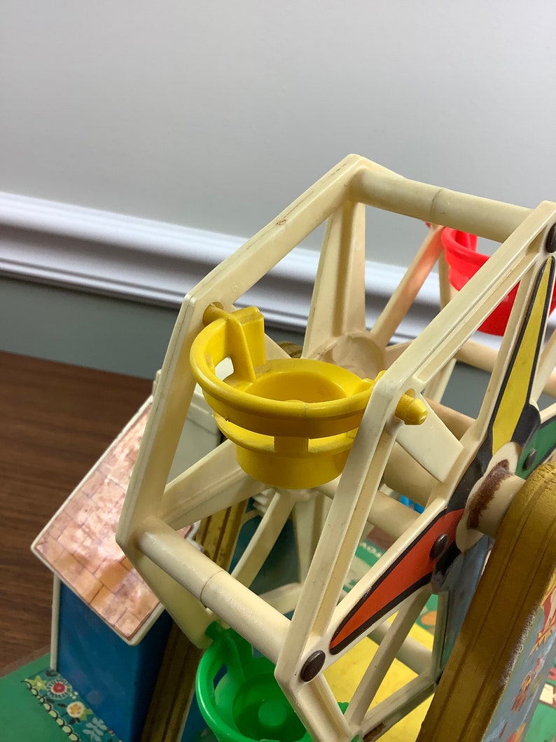 K&ouml;nnte beinhalten: Ein vintage Spielzeug-Riesenrad aus Plastik mit gelben, roten und gr&uuml;nen Sitzen. Das Rad ist wei&szlig; mit schwarzen Akzenten und Teil eines gr&ouml;&szlig;eren Spielsets.
