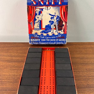 May include: Vintage game box with the word "SNIFF" in large, bold letters. The box is red, white, and blue with a cartoon illustration of three people. The game board is red with black pegs and is inside the box.