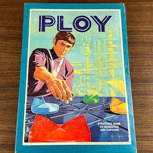 May include: A vintage board game box with a blue background and the word "PLOY" in large white letters. The box features a futuristic city scene and a man playing the game. The text on the box reads "Strategic Game of Maneuver and Capture" and "Copyright 1970 by 3M Company, St. Paul, Minnesota 55101."