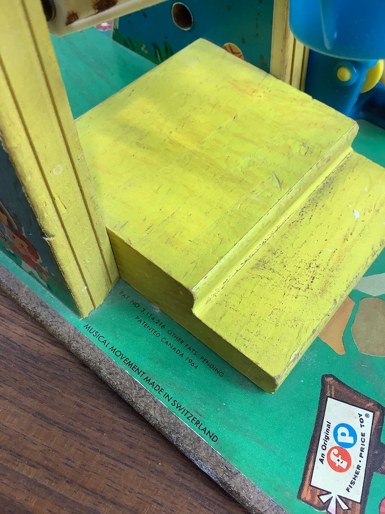 K&ouml;nnte beinhalten: Gelbes Holzspielzeug mit gr&uuml;nem Sockel und blau-gelbem Oberteil. Das Spielzeug hat ein musikalisches Spielwerk, das in der Schweiz hergestellt wurde. Der Text auf dem Sockel lautet "Pat. No. 3,114,216 Other Pats. Pending Patented Canada 1964 Musical Movement Made in Switzerland."