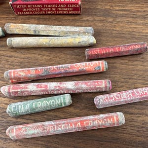May include: A collection of vintage Priscilla Crayon brand filters, with red and green packaging. The filters are cylindrical and show signs of age, with text visible on the packaging.