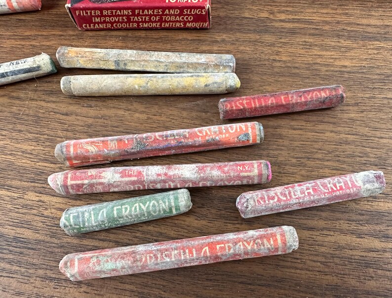 May include: A collection of vintage Priscilla Crayon brand filters, with red and green packaging. The filters are cylindrical and show signs of age, with text visible on the packaging.