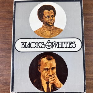 May include: A rectangular board game box titled Blacks & Whites with a gray background. The cover features two circular illustrations of individuals, one in a white circle and one in a black circle, with the game title printed in a central white oval.