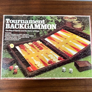 May include: A brown wooden backgammon game set with a folding board, dice, and playing pieces. The box features the text "Tournament Backgammon" and "The King of Games and the Game of Kings".