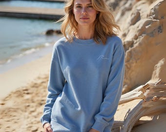 May include: A light blue sweatshirt with a white wave graphic on the front. The sweatshirt is made of a soft, comfortable material and has a relaxed fit.