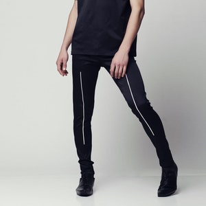 May include: A man wearing a black t-shirt with white and brown stripes on the sleeves, black pants with white stripes down the sides, and black shoes.