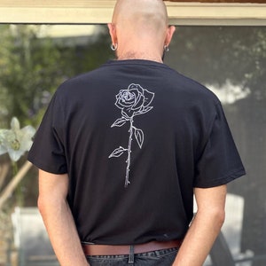 May include: A black t-shirt with a white outline of a rose on the back.