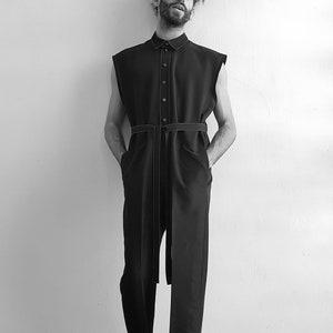 May include: A black sleeveless jumpsuit with a button-up front and a matching belt. The jumpsuit has white stitching details.