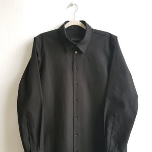 May include: A black long-sleeved button-down shirt with a collar and a label that reads "EURYDICE" on the inside of the collar.