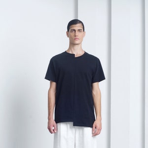 May include: A black t-shirt with a unique asymmetrical design and a white pair of cuffed shorts. The model is wearing black shoes.