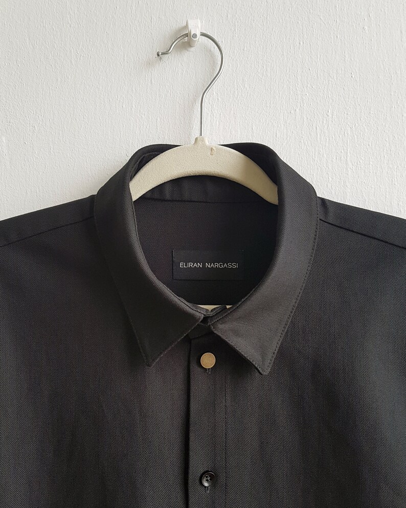 May include: A black collared shirt with a gold button and a label that reads "ELIRAN NARGASSI".