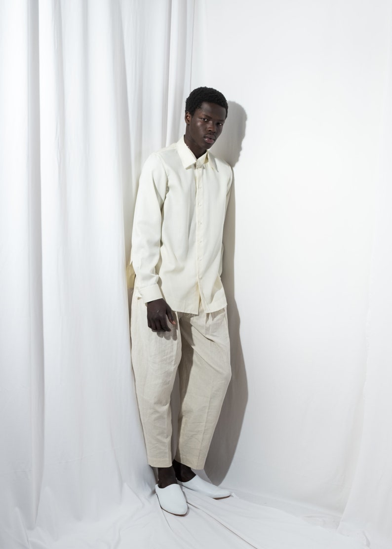 May include: A person wearing a white long-sleeved shirt and white pants. The person is standing in front of a white background.