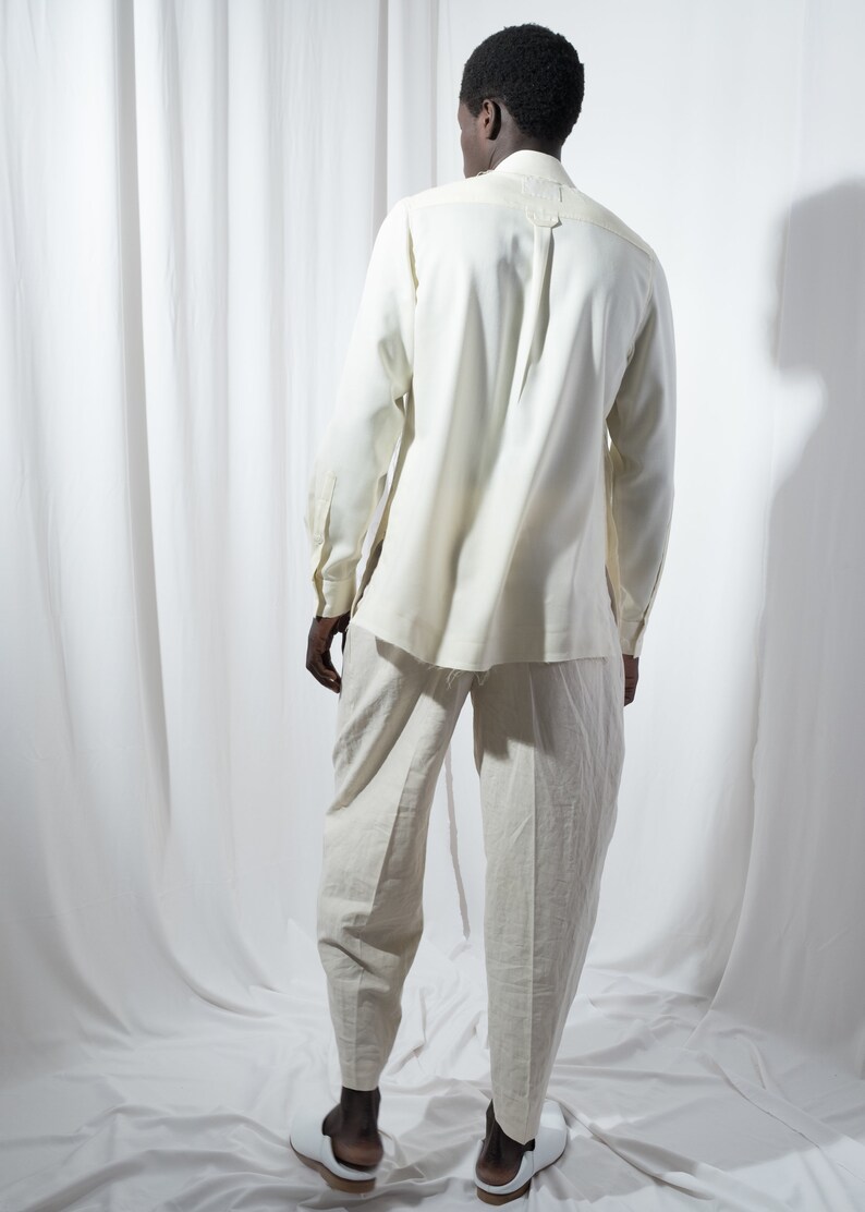 May include: A person wearing a white long-sleeved shirt and white pants. The person is standing in front of a white background.