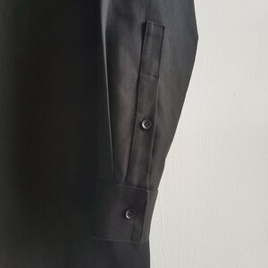 May include: Black long-sleeve shirt with a button cuff and a single button on the sleeve. The shirt has a plain design.