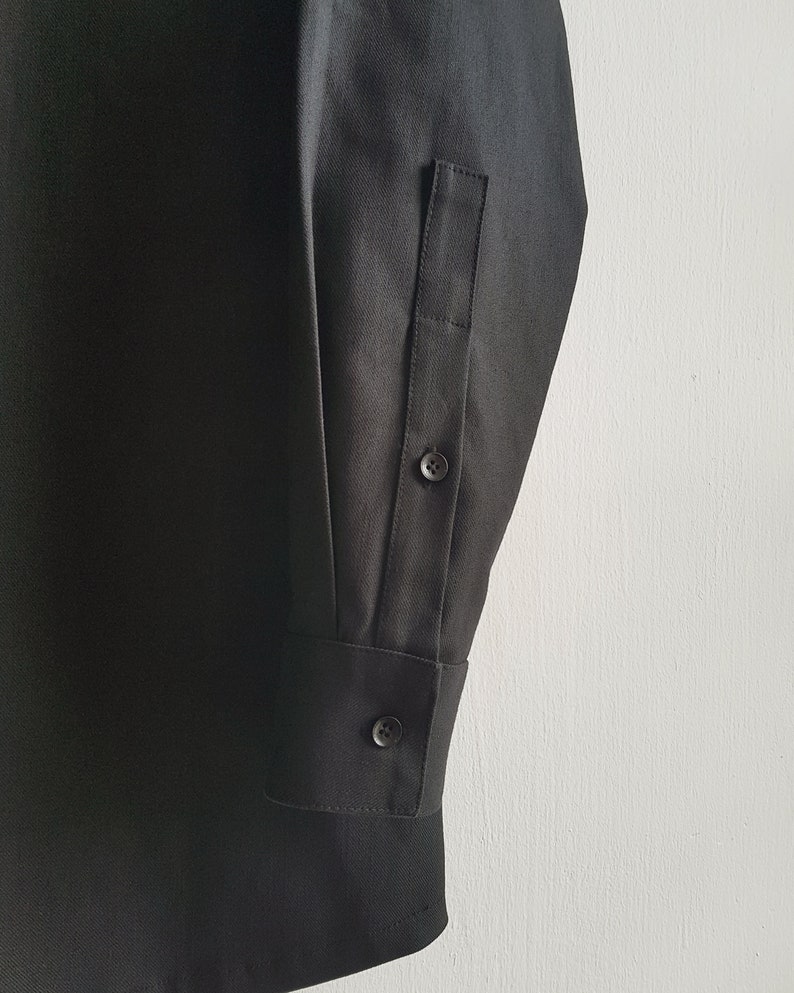 May include: Black long-sleeve shirt with a button cuff and a single button on the sleeve. The shirt has a plain design.