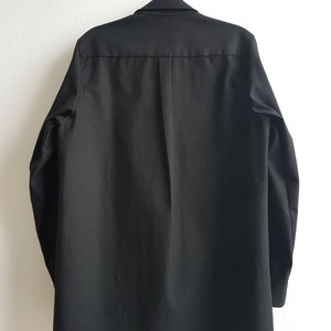 May include: A black long-sleeved button-up shirt with a collar and a single button closure at the top.