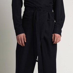 Puede incluir: Conjunto negro que presenta una camisa de manga larga y pantalones de cintura alta con cintur&oacute;n envolvente. Los pantalones tienen un dise&ntilde;o &uacute;nico con cierre de lazo y ojales met&aacute;licos. El atuendo est&aacute; hecho de una tela oscura de color s&oacute;lido.