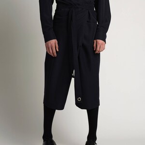 Puede incluir: Un conjunto azul marino oscuro con una camisa de manga larga y pantalones cortos tipo envolvente. Los pantalones cortos tienen un cintur&oacute;n que se envuelve alrededor de la cintura y un detalle de ojal met&aacute;lico. El atuendo se combina con medias negras y zapatos de cuero negros.