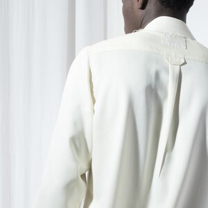 May include: A white long-sleeved shirt with a button-up collar and a single button at the top of the collar.