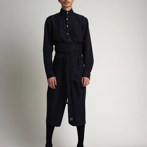 Puede incluir: Un conjunto azul marino compuesto por una camisa de manga larga con cuello mao y cierre de botones, combinada con unos pantalones culotte hasta la rodilla. Los pantalones culotte est&aacute;n envueltos en la cintura con un cintur&oacute;n de tela a juego. El conjunto se completa con medias negras y zapatos de cuero.