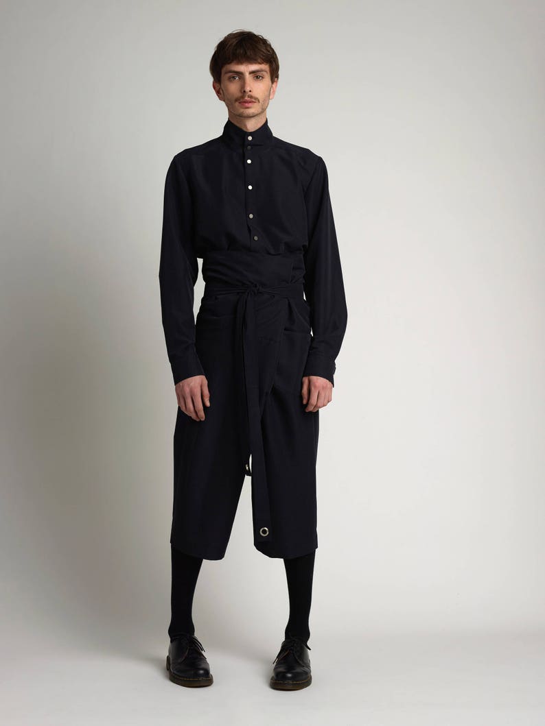 Puede incluir: Un conjunto azul marino compuesto por una camisa de manga larga con cuello mao y cierre de botones, combinada con unos pantalones culotte hasta la rodilla. Los pantalones culotte est&aacute;n envueltos en la cintura con un cintur&oacute;n de tela a juego. El conjunto se completa con medias negras y zapatos de cuero.