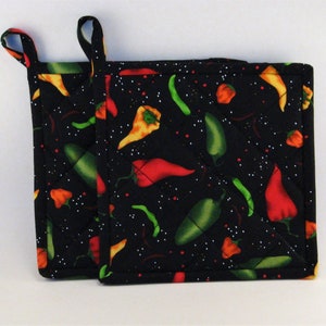 May include: Two black quilted hot pads with a chili pepper pattern. The hot pads have a loop handle and are decorated with red, green, and yellow chili peppers on a black background.