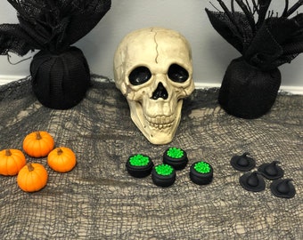 May include: A Halloween themed table setting with a skull, black pumpkins, green cauldrons, and black witch hats.