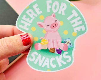 May include: A sticker with a pink pig illustration and the words "HERE FOR THE SNACKS". The pig is surrounded by snacks like a cupcake, chocolate, and crisps. The background is light green with yellow spots.