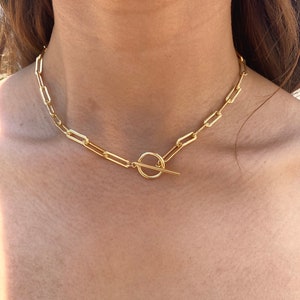 May include: A gold chain necklace with a toggle clasp. The chain is made of thick, linked rectangles.