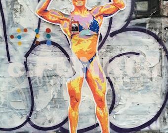 May include: A colorful image of a woman with a muscular physique, wearing a pink and blue bikini, posing with her arms raised. The image is set against a background of graffiti and peeling paint. The text "I'M B/ BILLI" is visible in a speech bubble above the woman's head.  The image also features several cans of Campbell's Cream of Mushroom Soup.