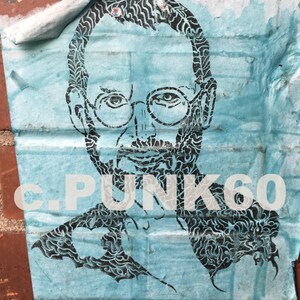 May include: A blue and black stencil of a person's face with the text "C.PUNK60" on the bottom. The stencil is on a brick wall.