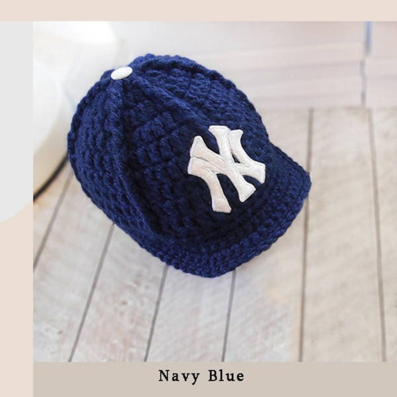 Puede incluir: Gorra de b&eacute;isbol de punto azul marino con el logotipo blanco "NY". La gorra tiene una visera curva y un bot&oacute;n en la parte superior. El texto "Navy Blue" est&aacute; en la parte inferior de la imagen. Un accesorio de moda.