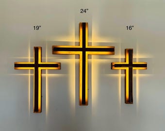 May include: Three wooden crosses with a warm, glowing light. The largest cross is 61 cm tall, the middle one is 48 cm, and the smallest is 41 cm. Each cross has a dark brown frame with a black stripe.