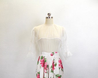May include: A white skirt with a floral print of pink roses and green leaves. The skirt is full and has a gathered waist.