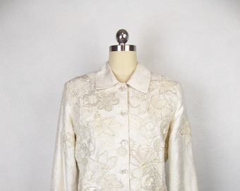 May include: A white button-up jacket with a floral design. The jacket is made of a silky material and has a collar.