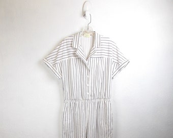 May include: A white and black striped jumpsuit with short sleeves and a collared neckline. The jumpsuit has a button closure and a cinched waist.