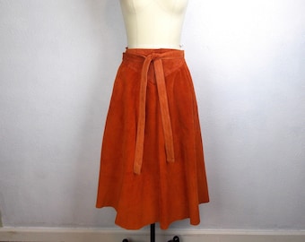 May include: A burnt orange suede skirt with a wrap-around tie belt. The skirt is knee-length and has a flared silhouette.