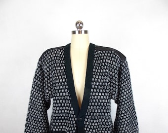 May include: A black and white patterned cardigan with a v-neck and button closure. The cardigan has two pockets and a textured knit.