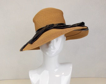 May include: A wide-brimmed straw hat with a black satin ribbon and bow. The hat is brown and has a slightly textured finish.