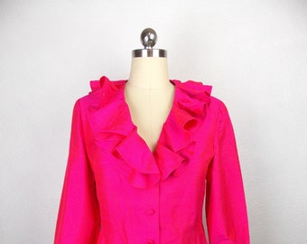 May include: A bright pink blouse with a large ruffled collar and long sleeves. The blouse has a button-up front.