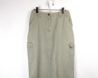May include: A khaki cargo skirt with two large pockets on the sides. The skirt is hanging on a white hanger against a white background.