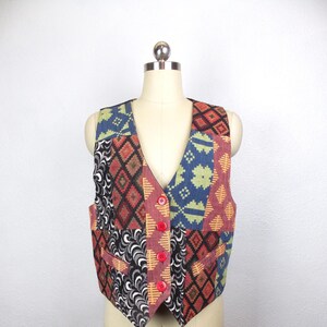 May include: A patchwork vest with a V-neck and red buttons. The vest features various geometric patterns in shades of red, blue, green, and black. The vest is displayed on a mannequin.