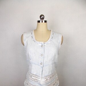 May include: A light blue denim vest with a white lace trim and button closure.