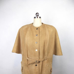 May include: A tan suede cape with a button-up front, a belt, and two pockets. The cape has short sleeves and a collar.