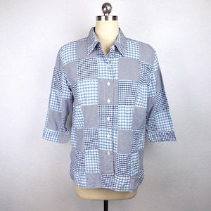 May include: A patchwork button-down shirt in shades of blue and white, displayed on a mannequin. The shirt features a variety of gingham and checkered patterns, with three-quarter sleeves and a classic collar.