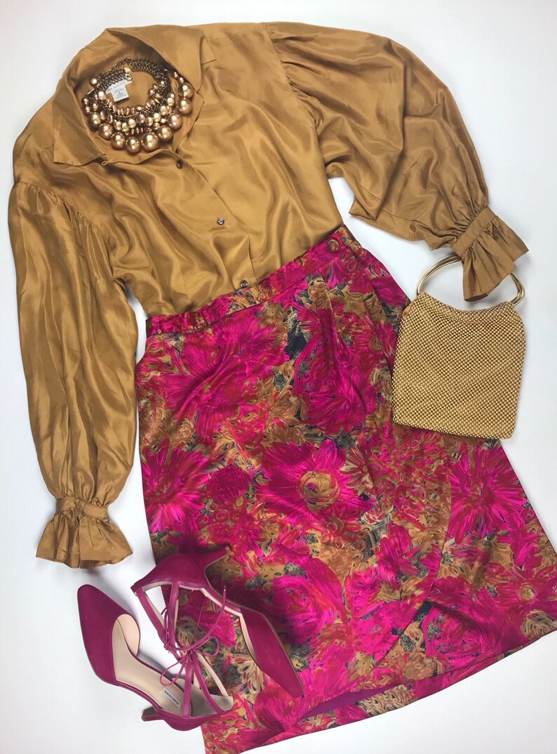 Pu&ograve; includere: Una blusa color senape con maniche lunghe e polsini a balze, una gonna rosa a fiori, una borsa a rete dorata e un paio di scarpe rosa con tacco.