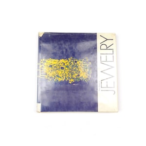 May include: A square book with a dark blue cover featuring a yellow abstract graphic design in the center. The word JEWELRY is printed in large, vertical, black capital letters on the right side, with the author name printed below it.