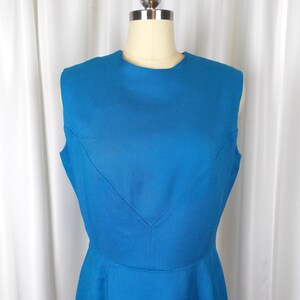 May include: A sleeveless, knee-length dress in a vibrant blue hue. The dress features a classic, tailored silhouette with a scoop neckline and a subtle V-shaped detail at the bodice. The fabric appears to have a textured weave.